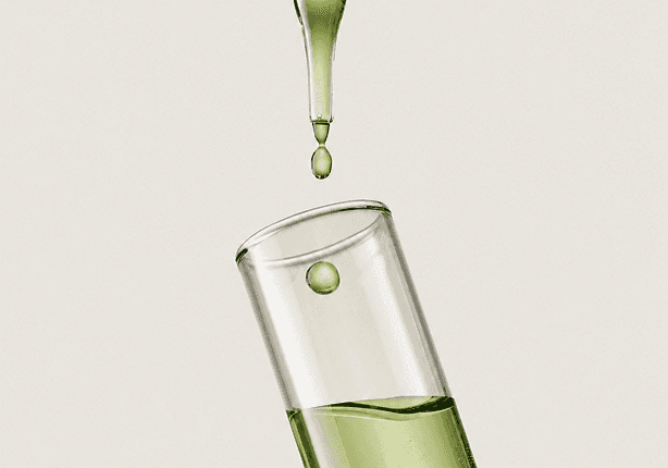 A green drop falling onto a test tube containing a plant-based liquid.